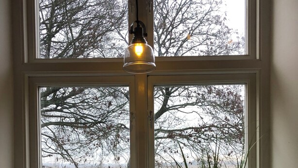 Une fenêtre avec un luminaire suspendu, une plante en pot et une petite lanterne posée sur le rebord de la fenêtre.