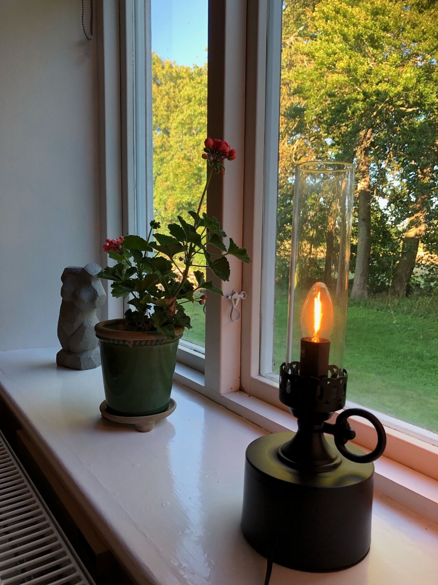 Un rebord de fenêtre orné d’un pot de fleurs, d’une petite statue et d’un chandelier.