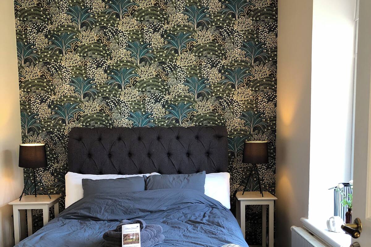 A bedroom with a tufted headboard, a bed with a blue bedspread, two bedside tables with lamps, and a radiator.