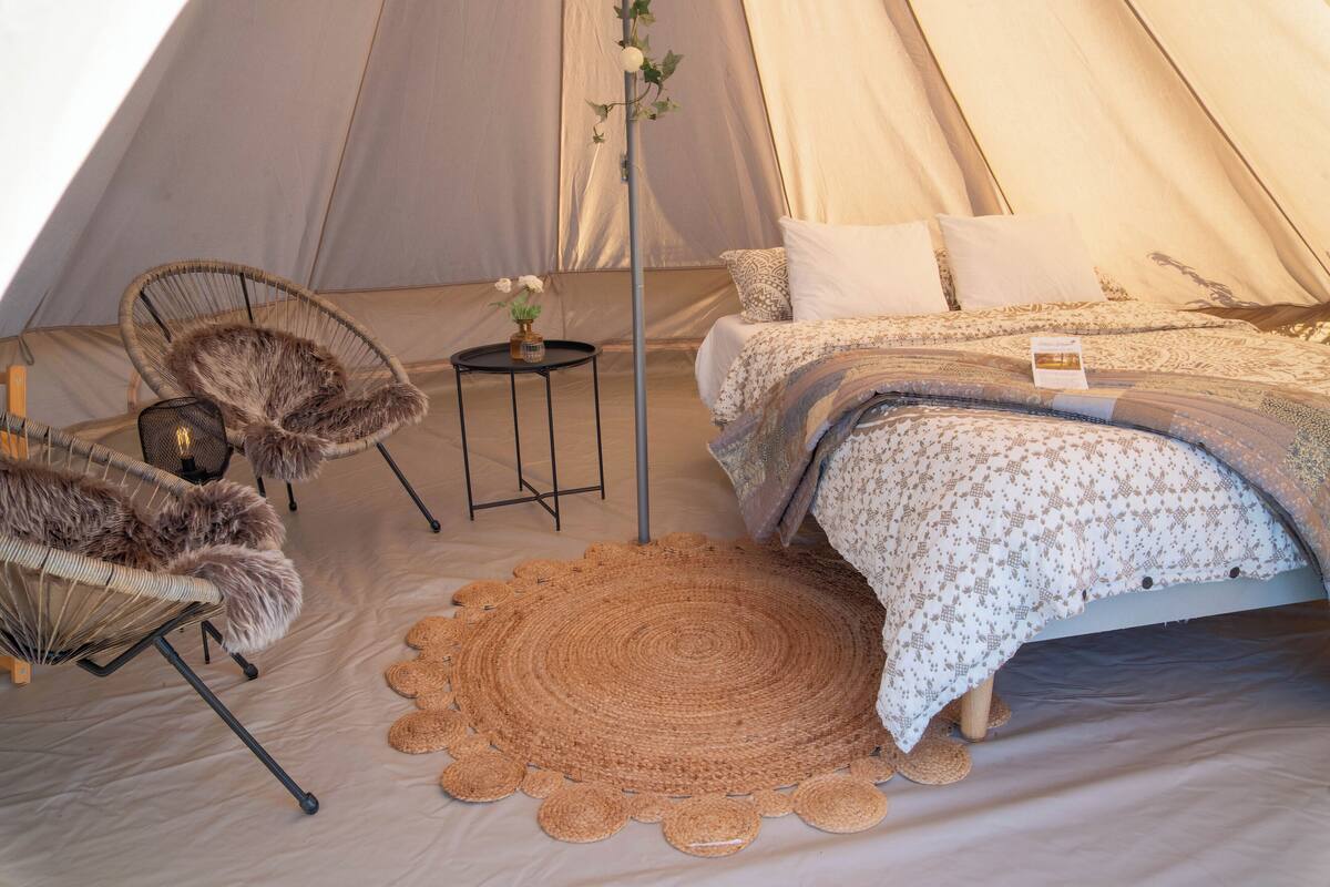 A tent with a bed, two chairs, a small table, and a decorative mat.