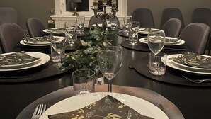 Une salle à manger élégante, avec une table dressée pour quatre personnes, agrémentée d’un chandelier avec des bougies, de verres transparents et de serviettes ornées de motifs floraux.