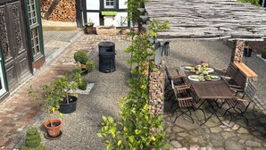 A traditional half-timbered building with a stone patio, a barbecue grill, and a table set for dining. - Vacation apartment/house with 2 bedrooms in the historic Vierkanthof (Mechernich)