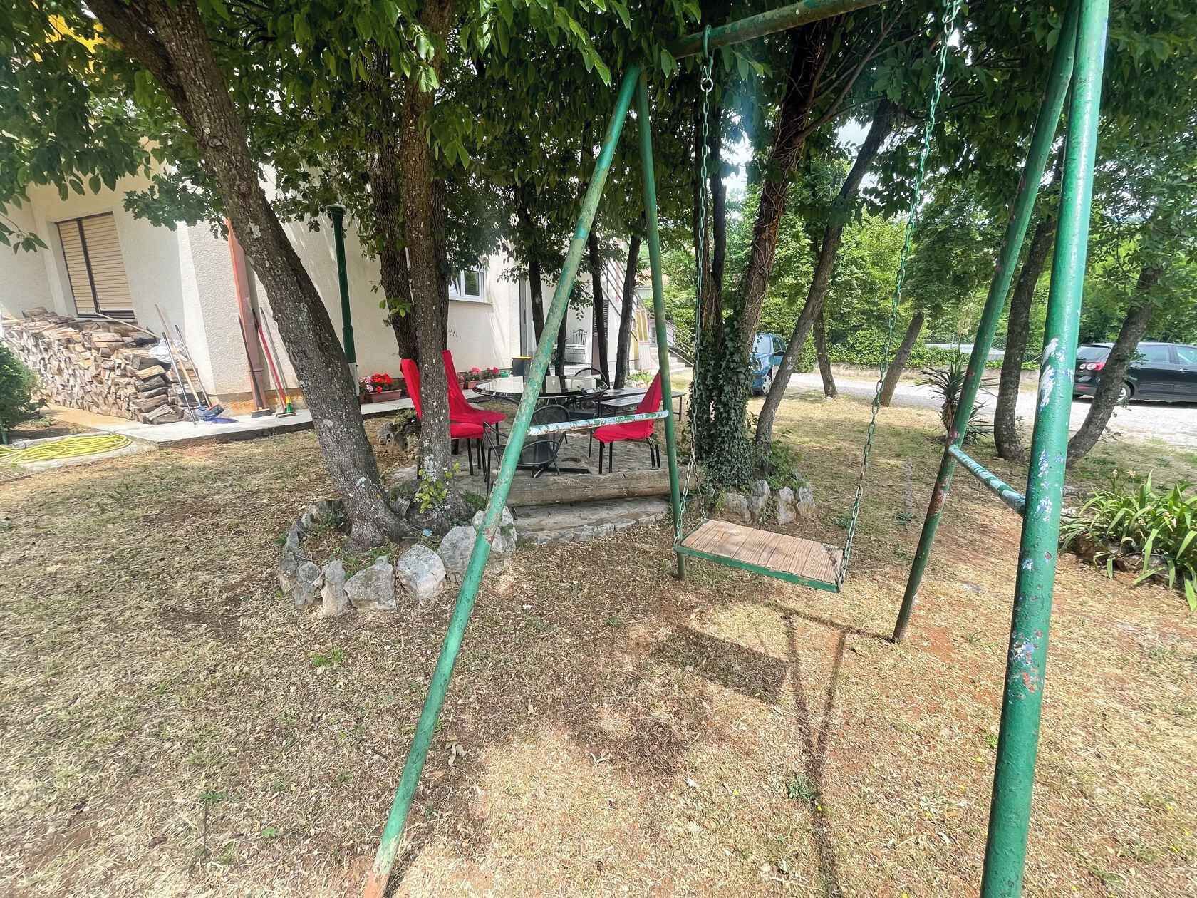 Eine Terrasse mit Schaukel, roten Stühlen und einem Tisch.