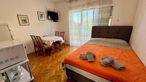 Quarto de hotel com cama, escrivaninha com cadeira, televisão e janela com cortinas.