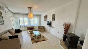Uma sala de estar com sofá, mesa de centro, televisão e um vaso decorativo.