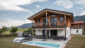 A two-story wooden house with a balcony, a swimming pool, and a view of the surrounding landscape. - 6 persons Chalet Bergherzerl in the Chiemgau. Summer pool, whirlpool & sauna (Inzell)