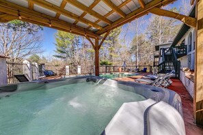 A hot tub under a wooden pergola with a pool in the background, surrounded by trees and a fenced area. - Kies Poolside Mountain Villa| Prime Location (Sautee Nacoochee)