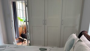 A bedroom with a bed featuring a leaf pattern, a wardrobe, and a view of a dog outside.