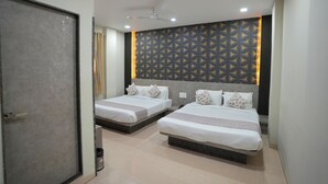 A hotel room with two beds, a ceiling fan, recessed lighting, and a patterned wall. - RRA Retreat Hotel (Nathdwara)