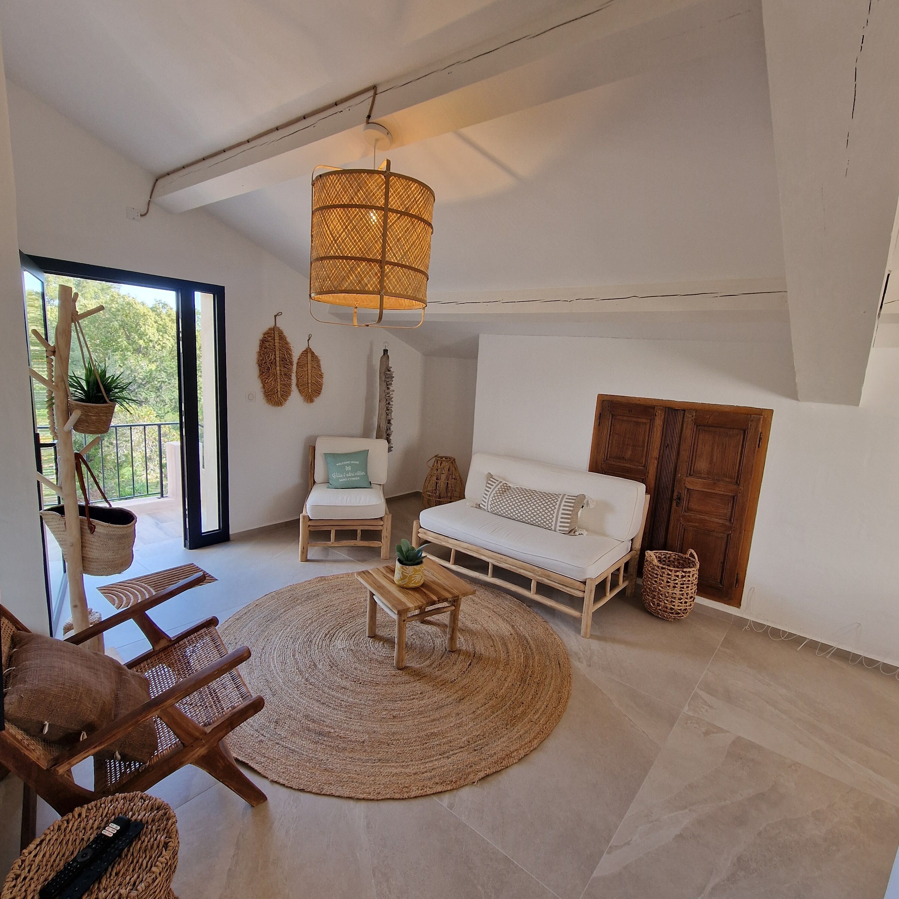 Un salón amplio con un gran ventanal, una lámpara colgante, un sofá, un sillón y una mesita.
