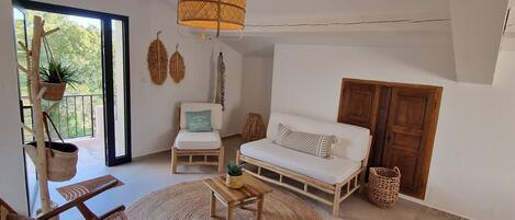 Un salón amplio con un gran ventanal, una lámpara colgante, un sofá, un sillón y una mesita.