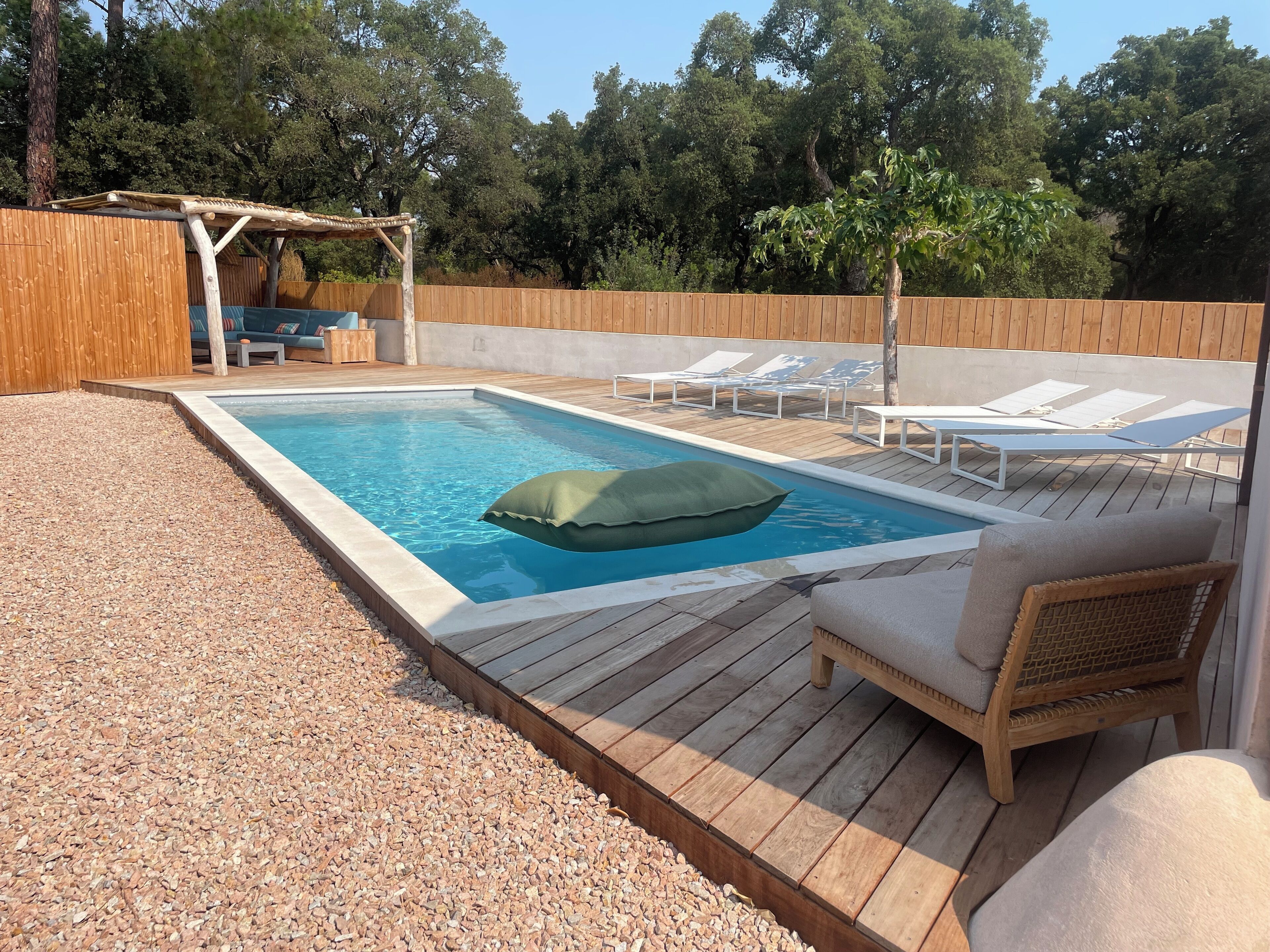 En rektangulär swimmingpool med ett trädäck runt om, utrustad med solstolar och en pergola.