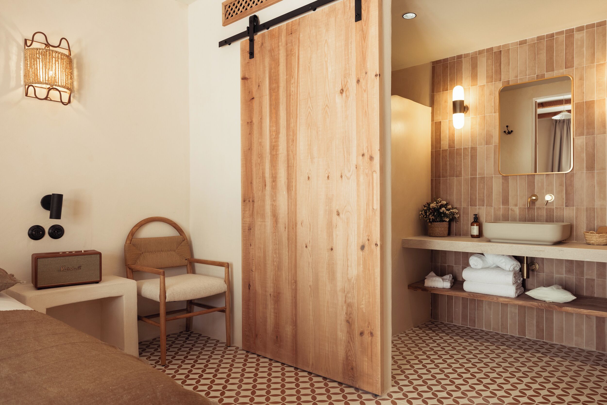 A modern bathroom with a wooden sliding door, a large mirror, a sink, and a patterned floor.