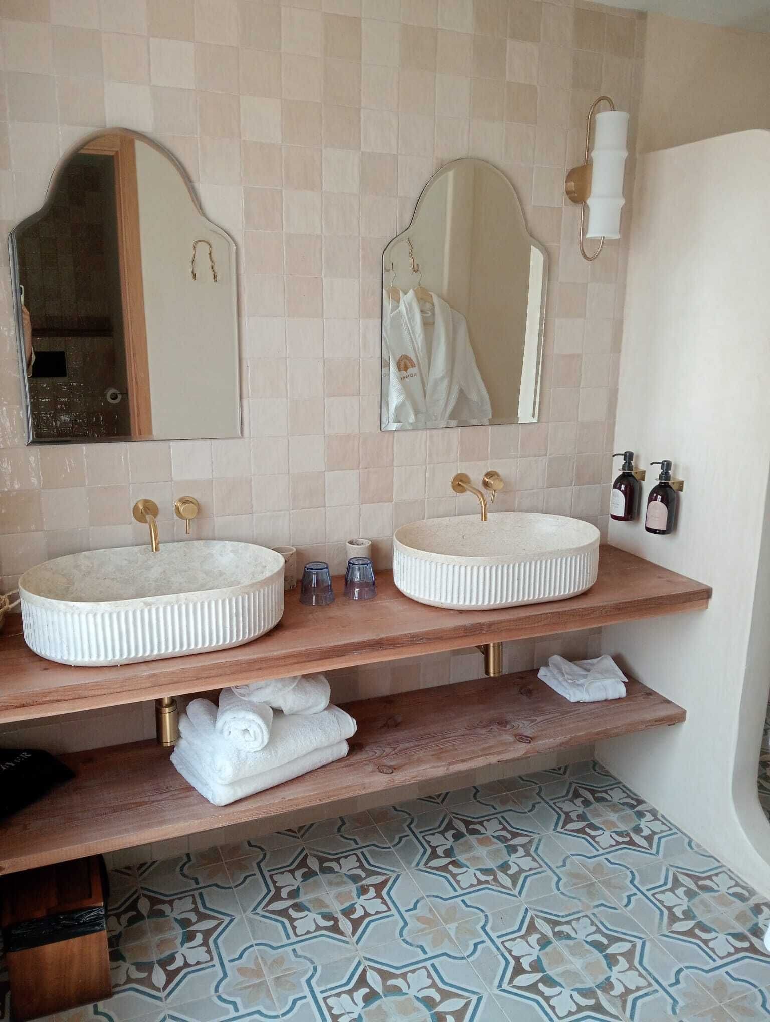 A bathroom with two round sinks, a mirror above each, and a towel rack. There are two bottles of soap on the right side.