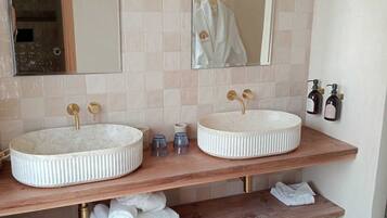 A bathroom with two round sinks, a mirror above each, and a towel rack. There are two bottles of soap on the right side.