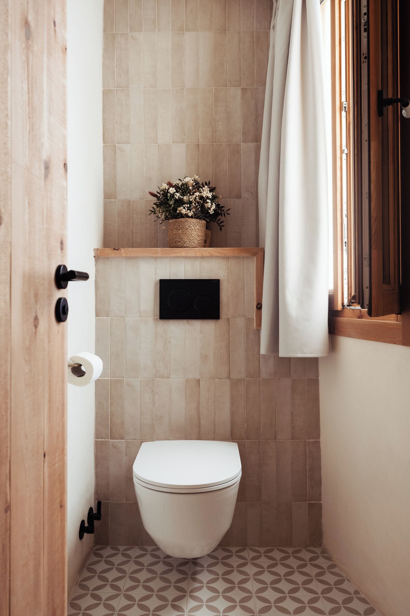 Un baño pequeño con inodoro, un estante de madera con una cesta de flores y una cortina de ducha.