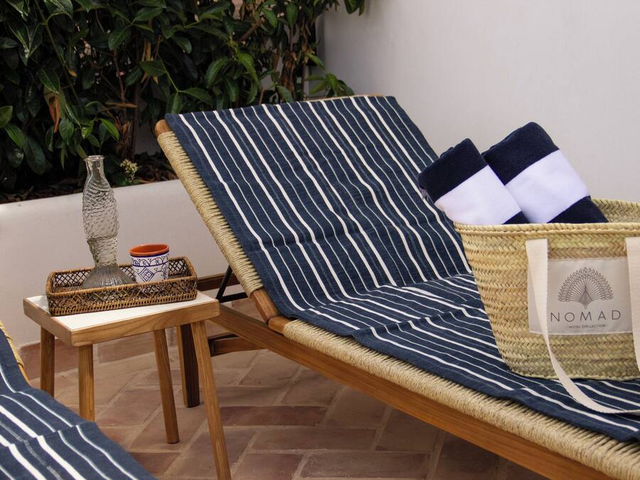 A striped lounge chair with a woven basket containing a bag and two folded towels.