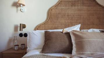 A neatly made bed with a woven headboard, a bedside lamp, and two decorative vases on a wooden nightstand.