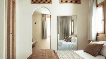 Une chambre à coucher avec un grand lit, un miroir, une armoire et une salle de bain visible à travers une arche.