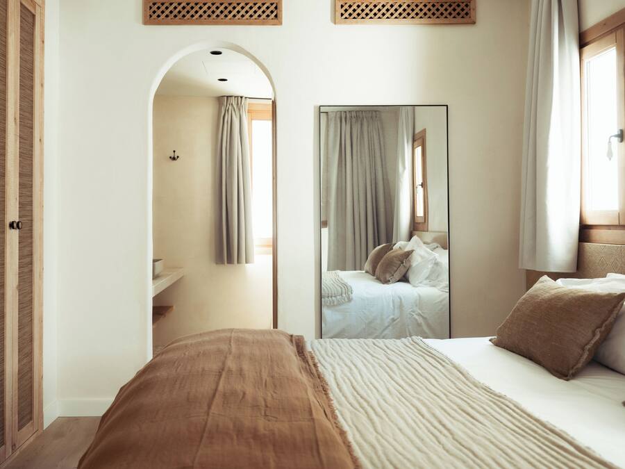 Une chambre à coucher avec un grand lit, un miroir, une armoire et une salle de bain visible à travers une arche.