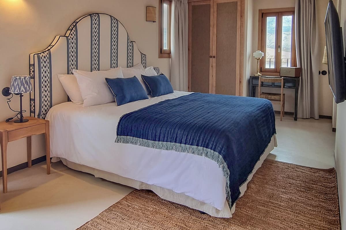 A bedroom with a bed, bedside table, lamp, and a desk with a chair.