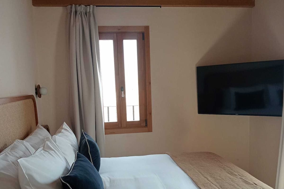 A bedroom with a bed, pillows, a window, and a TV.