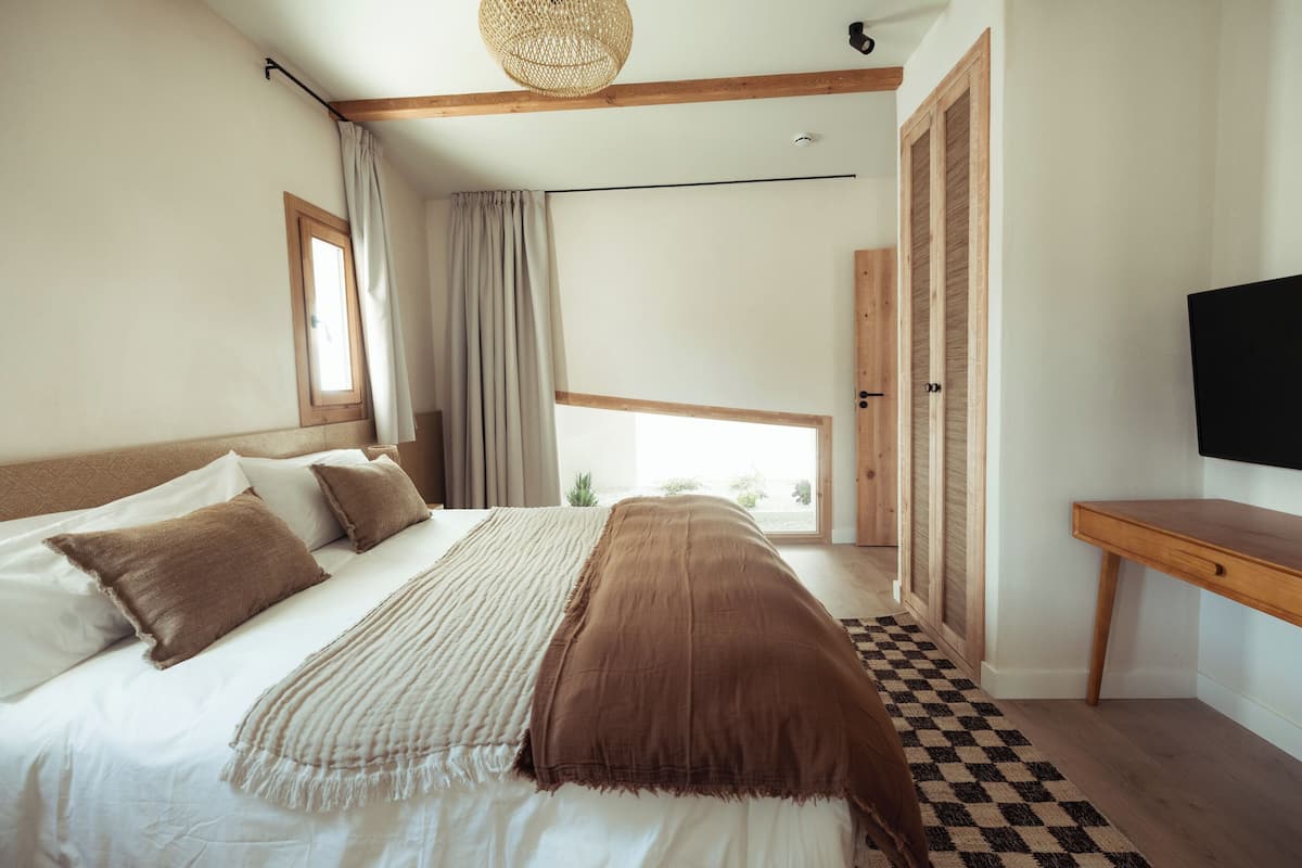 A bedroom with a large bed, a wooden desk, a television, and a window with curtains.