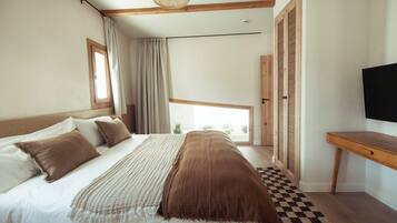 Un dormitorio con una cama grande, un escritorio de madera, una televisión y un ventanal con cortinas.