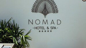 A wall with a logo and name for Nomad Hotel & Spa, a potted plant, and a table with chairs. - Nomad Hotel & Spa Altea (Altea)