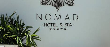 A wall with a logo and name for Nomad Hotel & Spa, a potted plant, and a table with chairs.