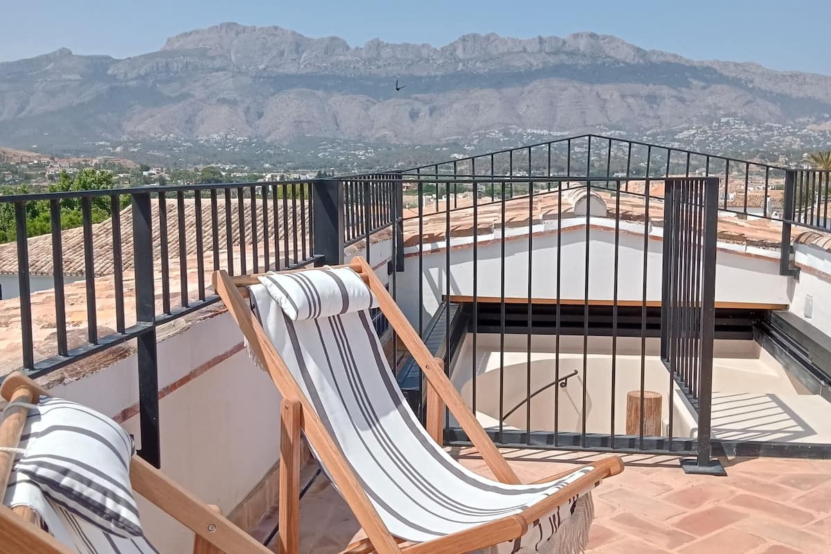 A terrace with two striped lounge chairs, a small table, and a view of mountains.