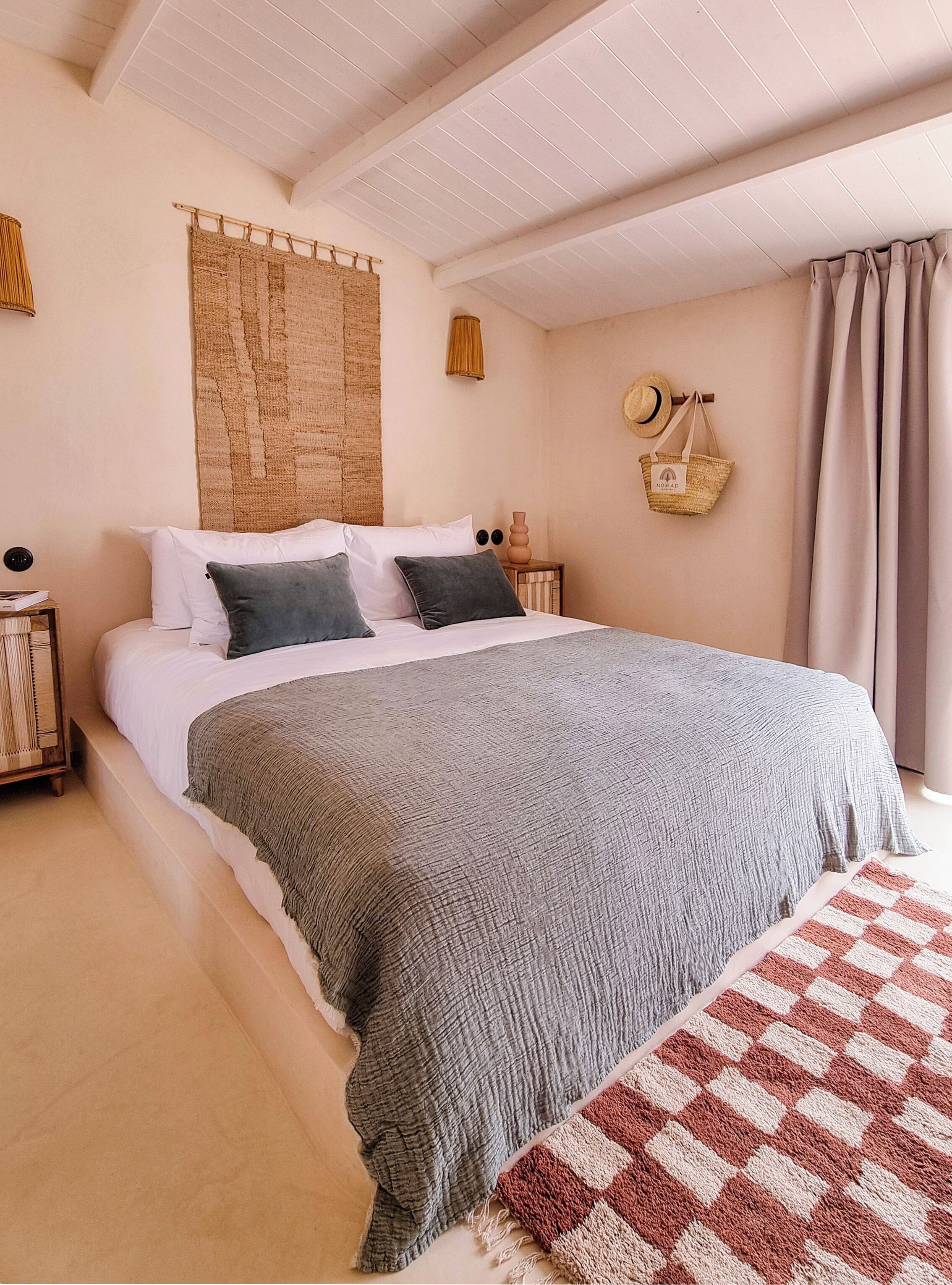 A bedroom with a large bed, a woven tapestry, a straw hat, and a woven basket on the wall.
