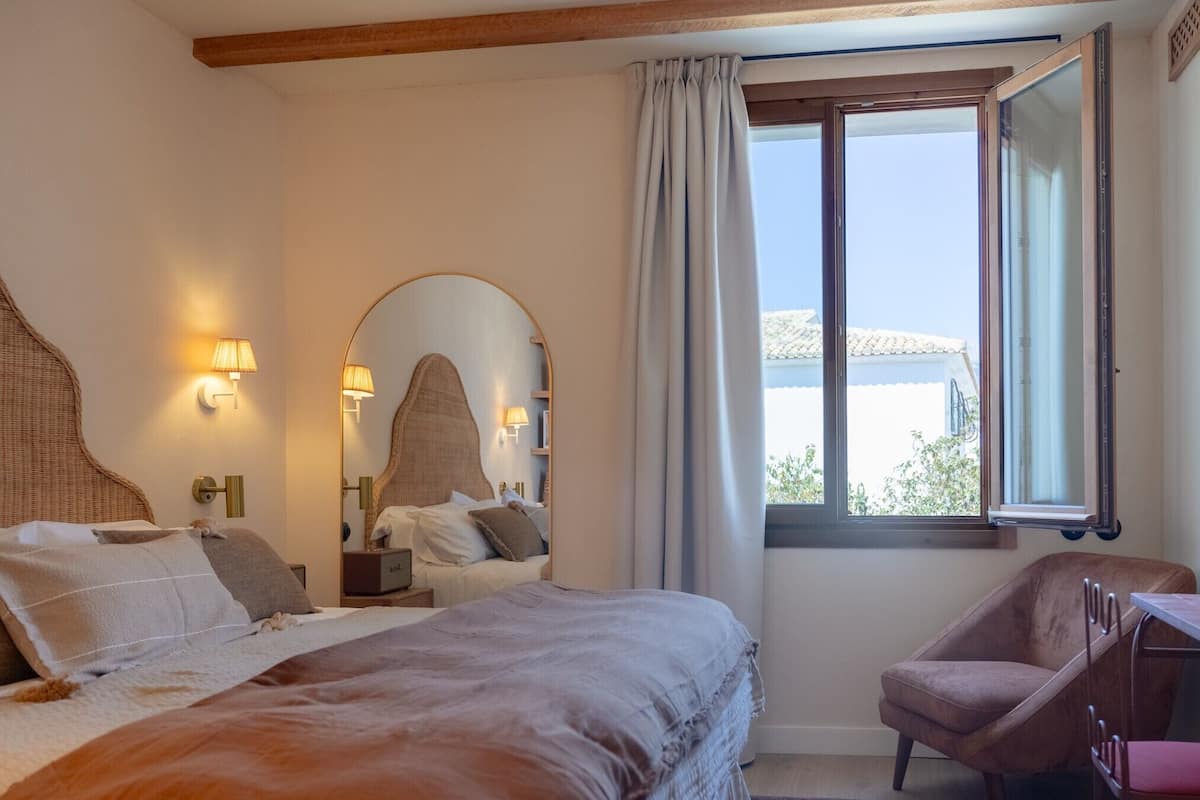 A bedroom with a large bed, a chair, a desk, and a window with a view.