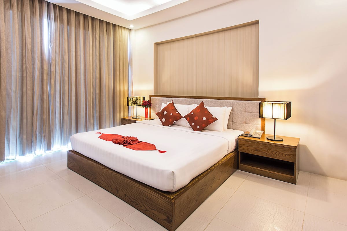 Una habitación de hotel moderna con una cama grande, cabecera de madera y una mesita de noche con lámpara.