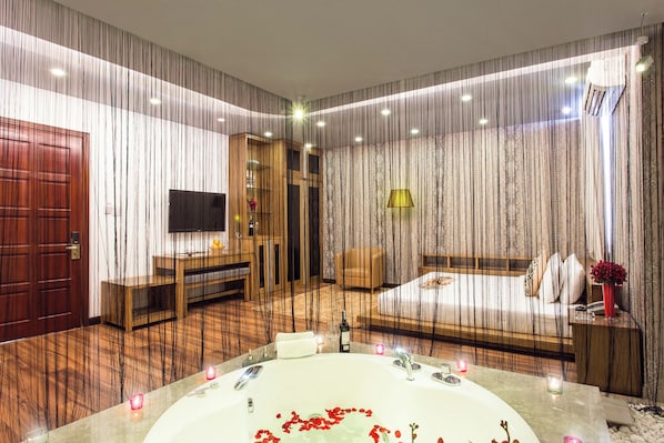 A modern bedroom with a large bathtub, a wooden desk, a television, and a bed with a nightstand. - VALENTINE HOTEL (Ho Chi Minh City)