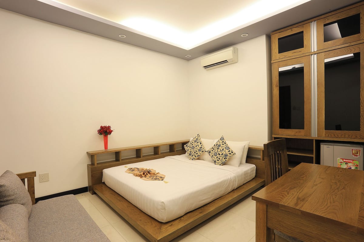 Un dormitorio con cama, mesita de noche, silla y una pequeña mesa con refrigerador.