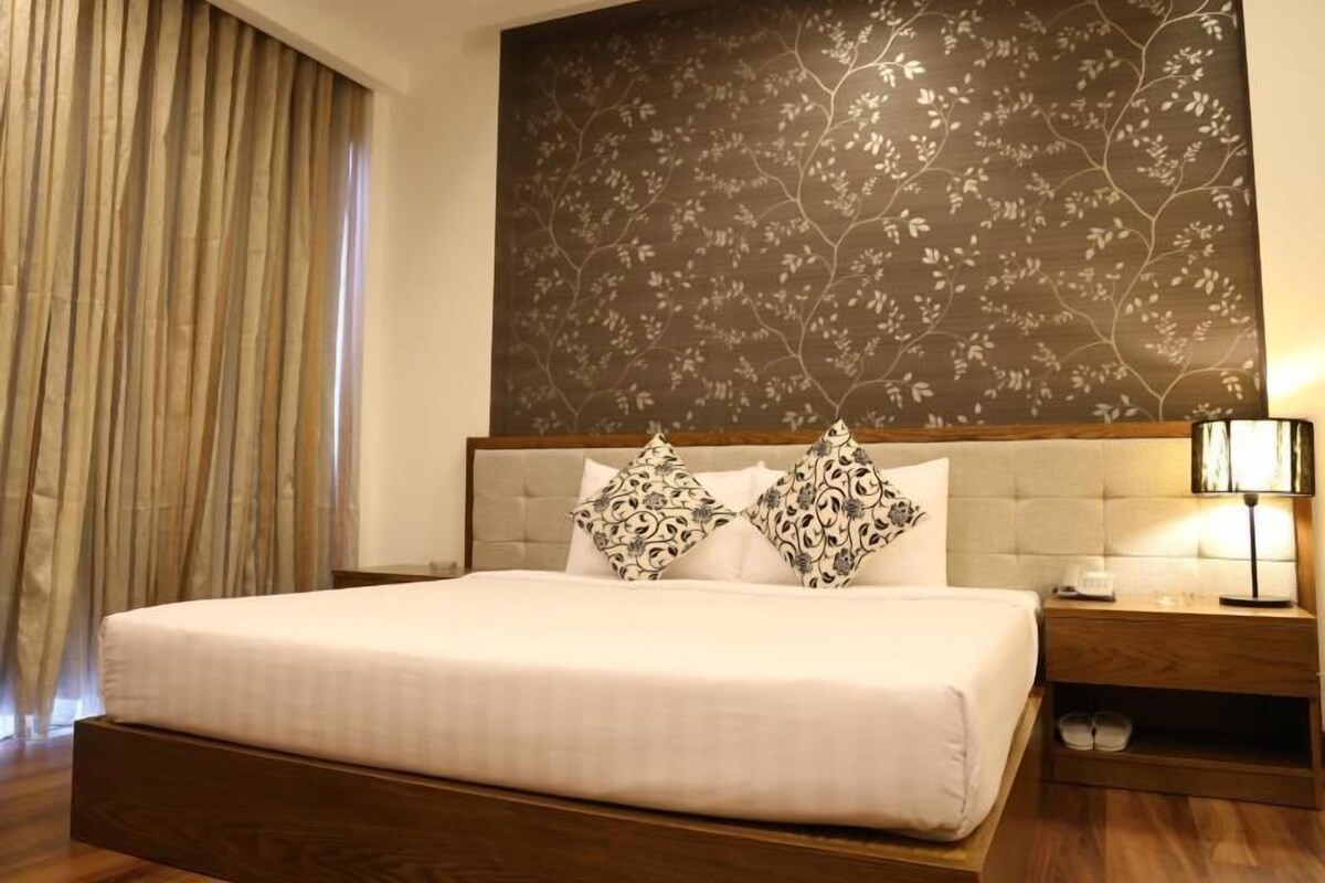 A hotel room with a large bed, a nightstand, a lamp, and a window with curtains.