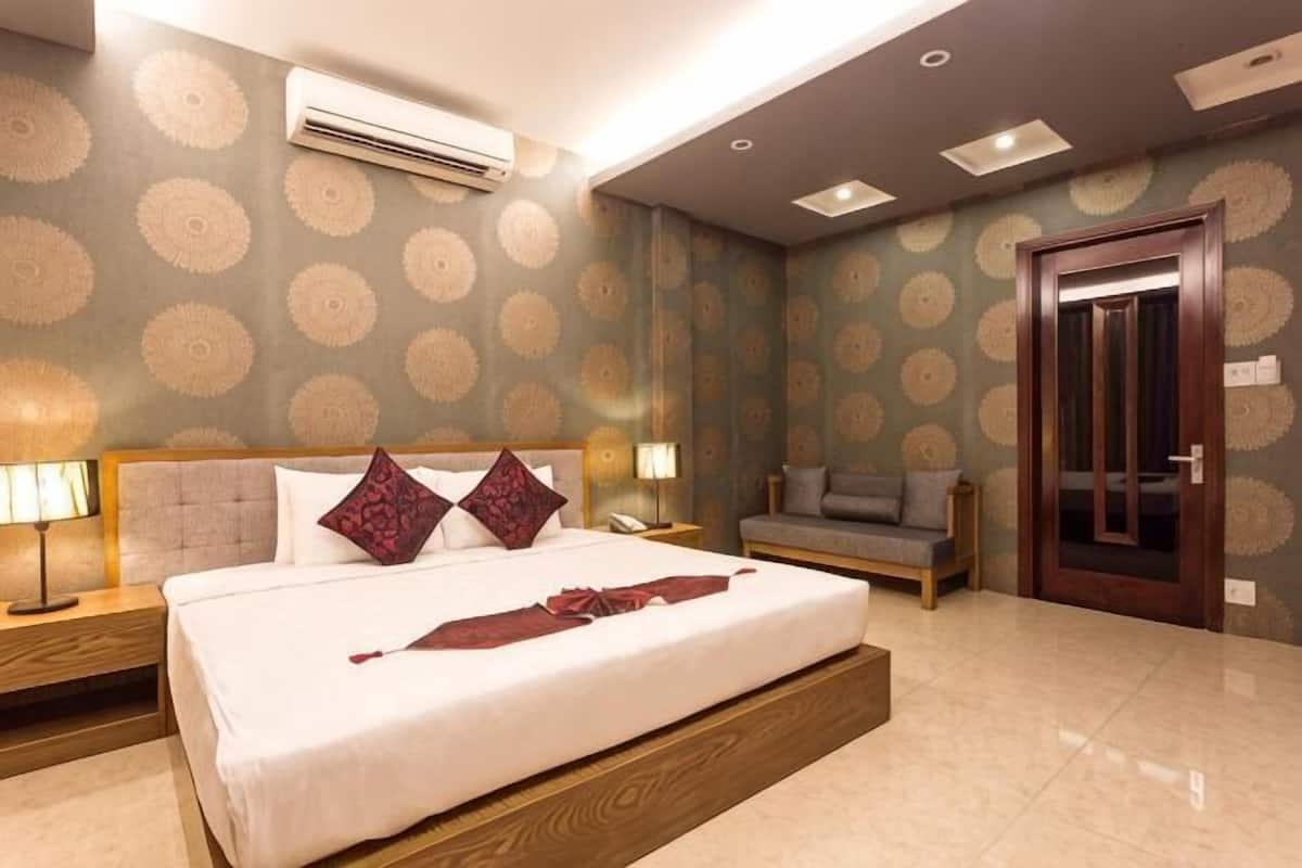 Una habitación de hotel con una cama grande, un sofá, un cabecero de madera, una mesita de noche y una puerta.