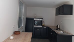 A compact kitchen with a built-in oven, a sink, and black cabinets. There is a wooden table with a white apple and a wicker basket.