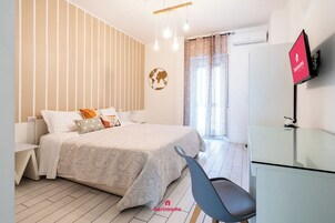 Una camera da letto moderna con un letto, un comodino e una sedia. C'è una televisione a parete e una finestra con tende.