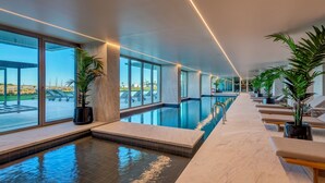 Una piscina interna moderna con pareti in vetro trasparente, sedie a sdraio e piante in vaso.