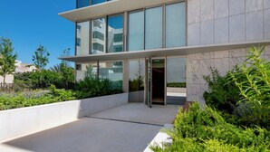 Un edificio moderno con ingresso in vetro, il numero '62' sulla parete e un’area verde con arbusti.