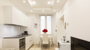 A modern kitchen with white cabinets, a dining table with chairs, a small refrigerator, and a TV on a stand. - notaMi - Campus Bligny Bocconi District (Milan)