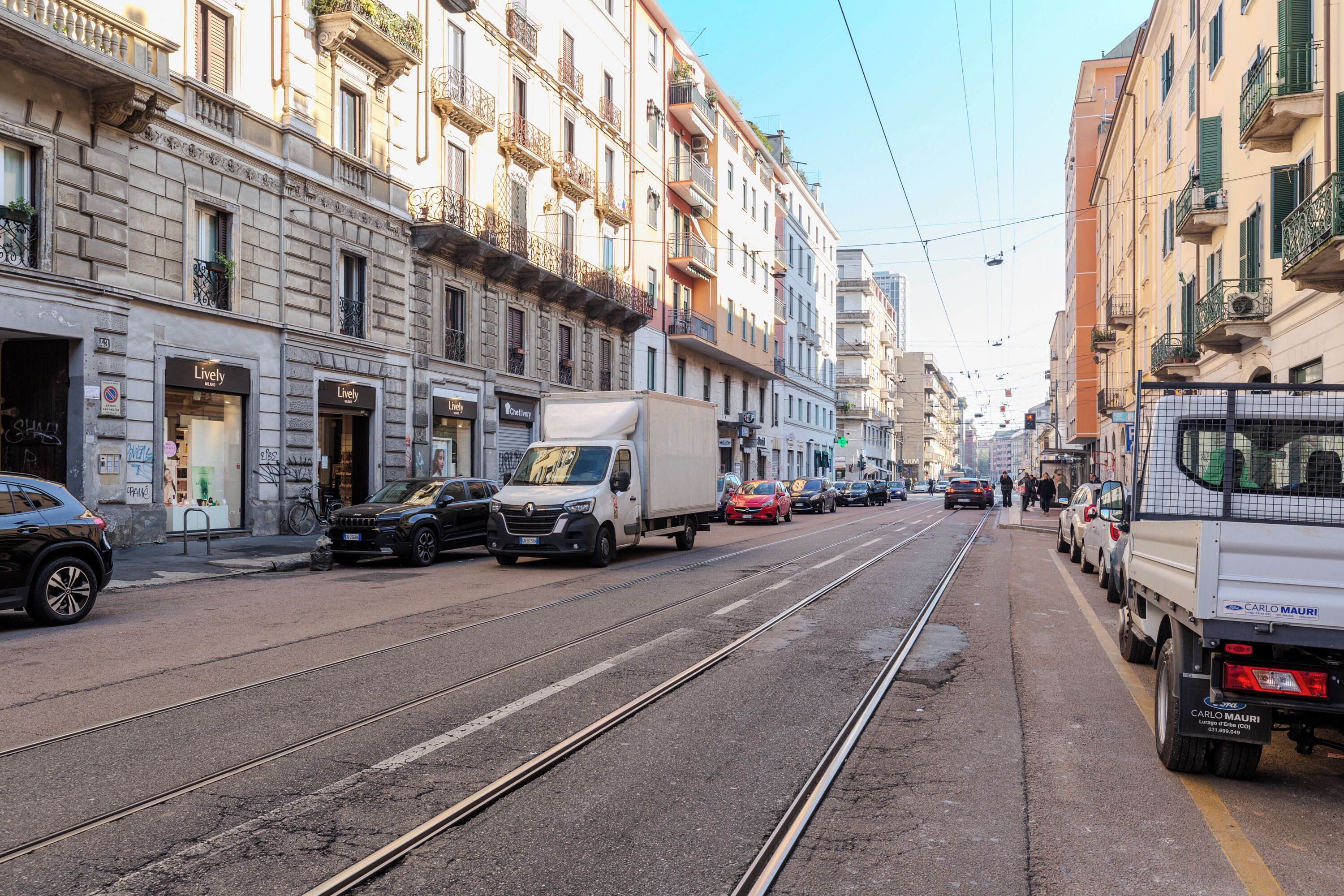 Eine Straße mit Straßenbahnschienen, parkenden Autos und Gebäuden mit Balkonen.