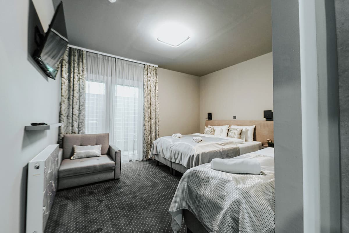 A hotel room with two beds, a sofa, a TV mounted on the wall, and a ceiling light.