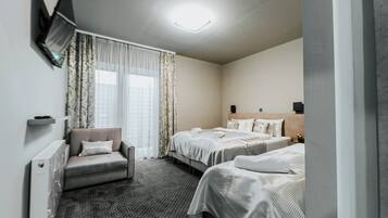 A hotel room with two beds, a sofa, a TV mounted on the wall, and a ceiling light.