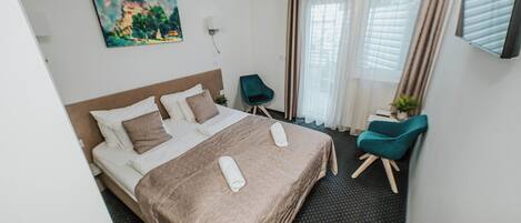 A hotel room with a bed, a chair, a painting, and a TV.