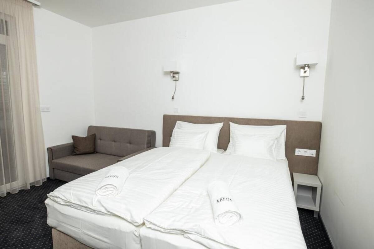 A hotel room with a bed, a sofa, and two wall-mounted lights.