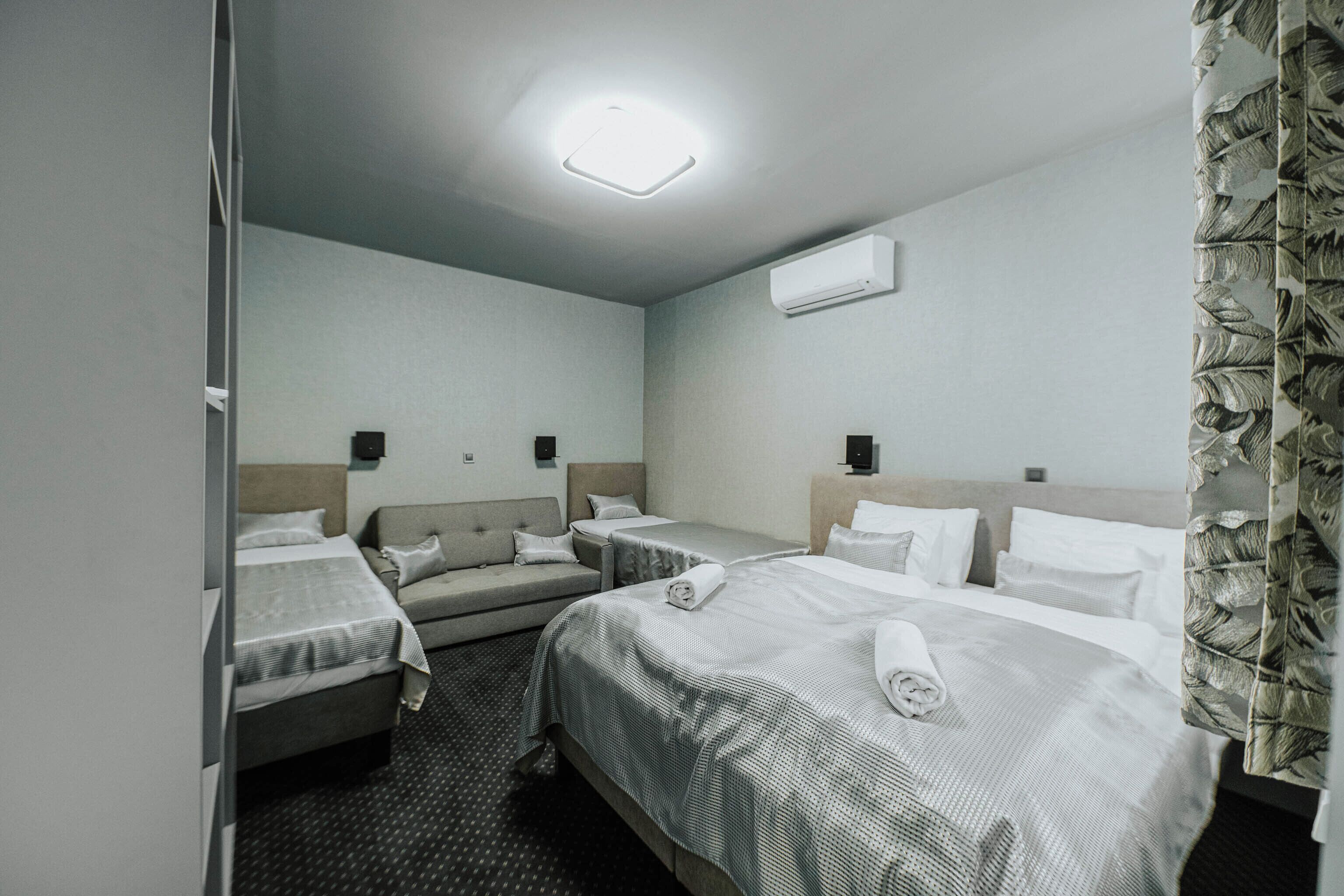 A hotel room with two beds, a sofa, a flat-screen TV, and a ceiling light.