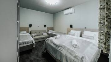A hotel room with two beds, a sofa, a flat-screen TV, and a ceiling light.
